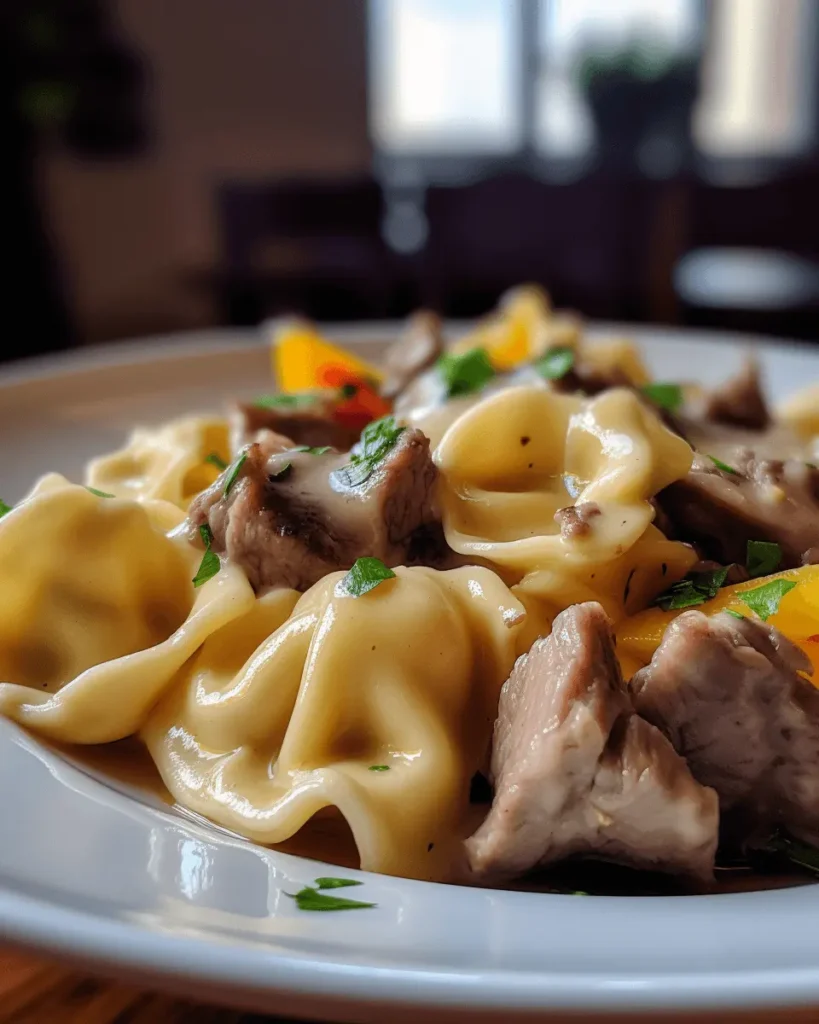 Classic Philly Cheesesteak Tortellini with tender steak, melted provolone cheese, and sautéed onions on a white plate.